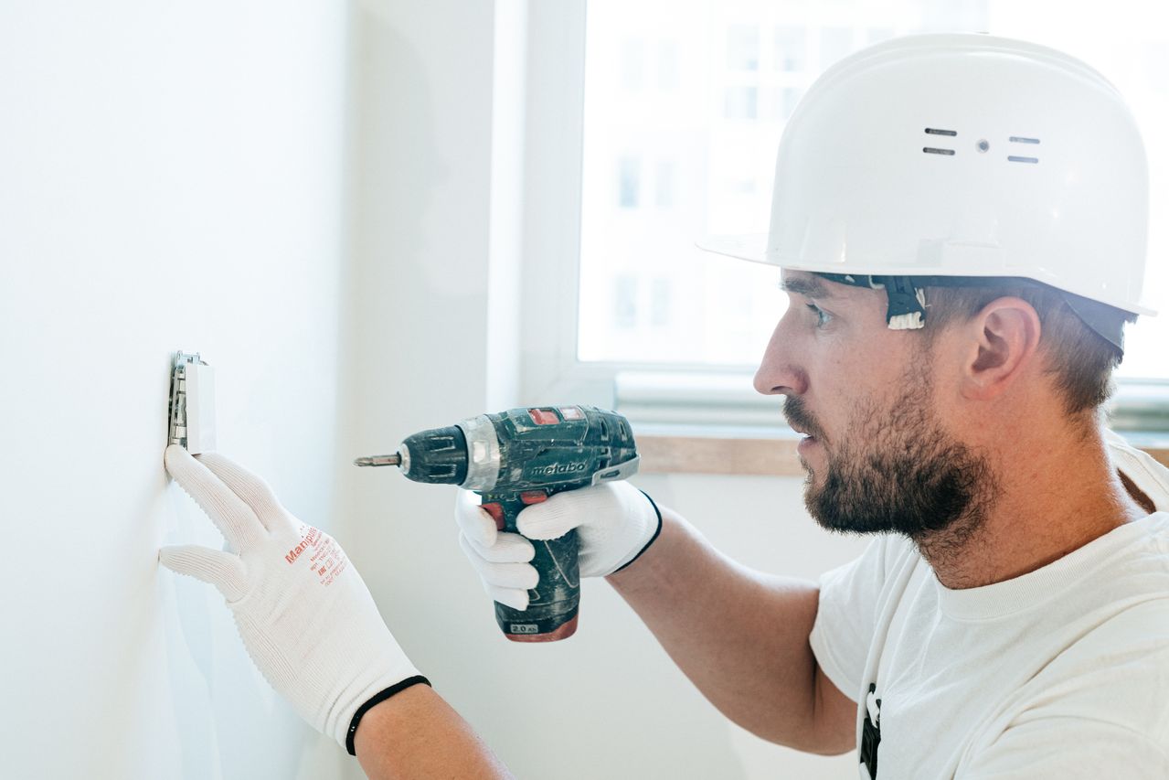 Handwerker mit Schutzhelm beim Bohren in eine Wand mit einer Akkubohrmaschine.